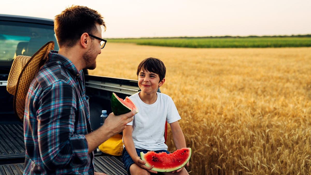 A father and son eat watermelon together.