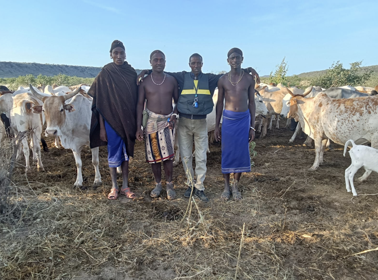 Four people stand together with sheep in a field.
