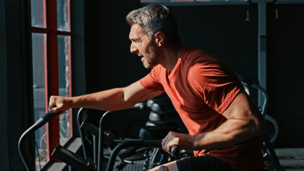 An older adult man performs a high-intensity workout on a stationary bike at a gym