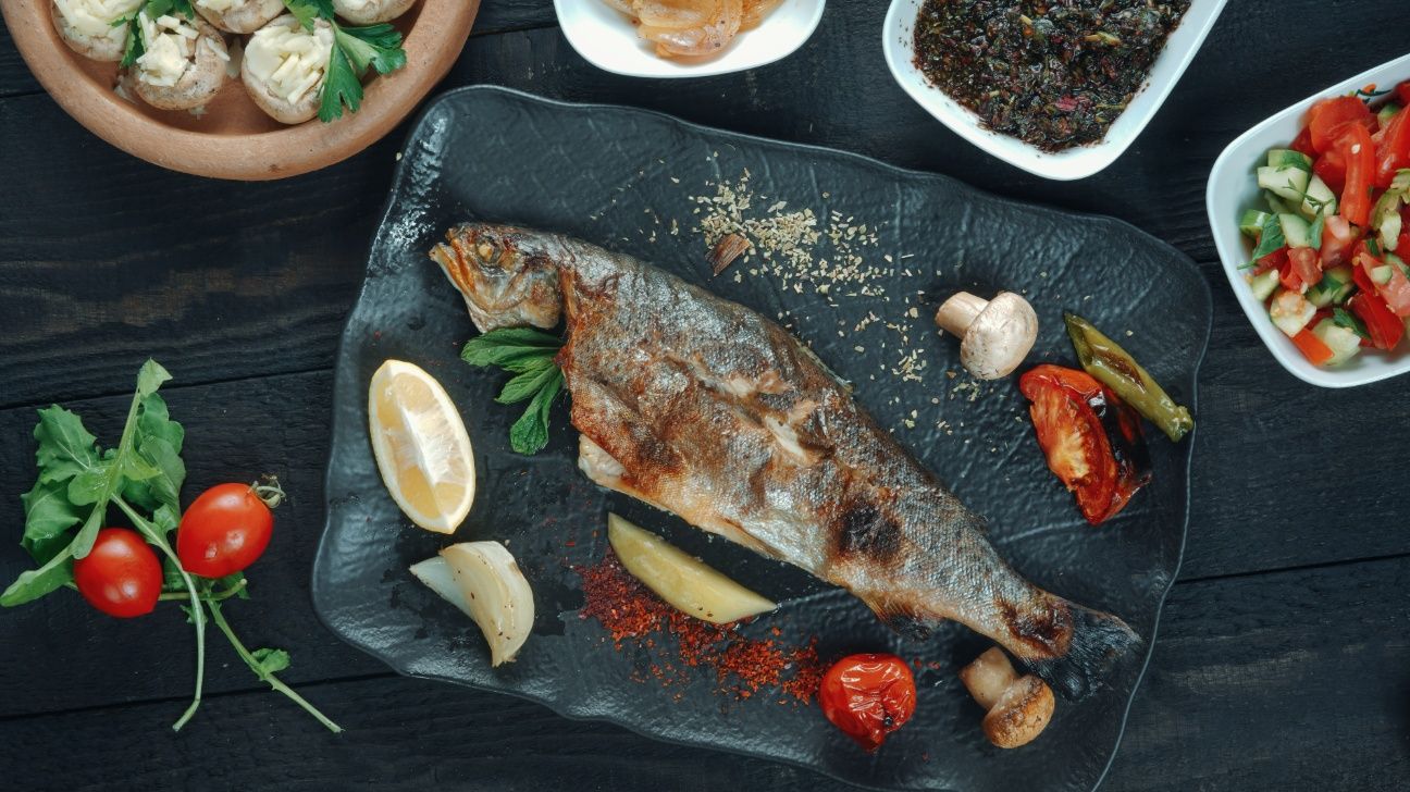 A whole fish surrounded by lemons, tomatoes, and vegetables