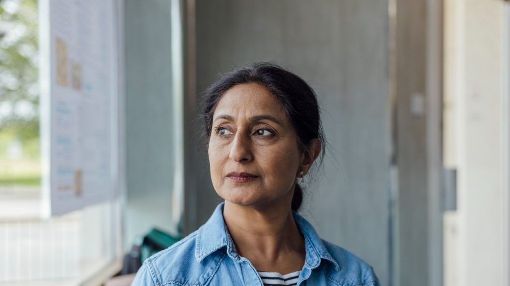 An adult woman around menopause age looks out of a window
