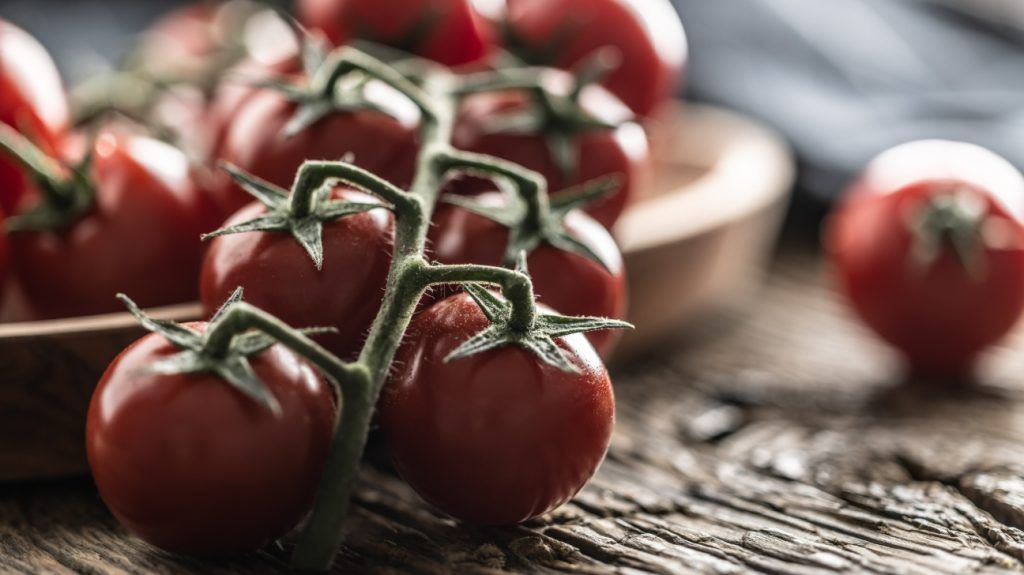 Fresh cherry tomatoes in a wooden bowl on a rustic oak table