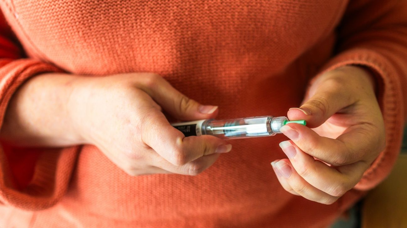 Female in an orange sweater holding a GLP-1 injection pen