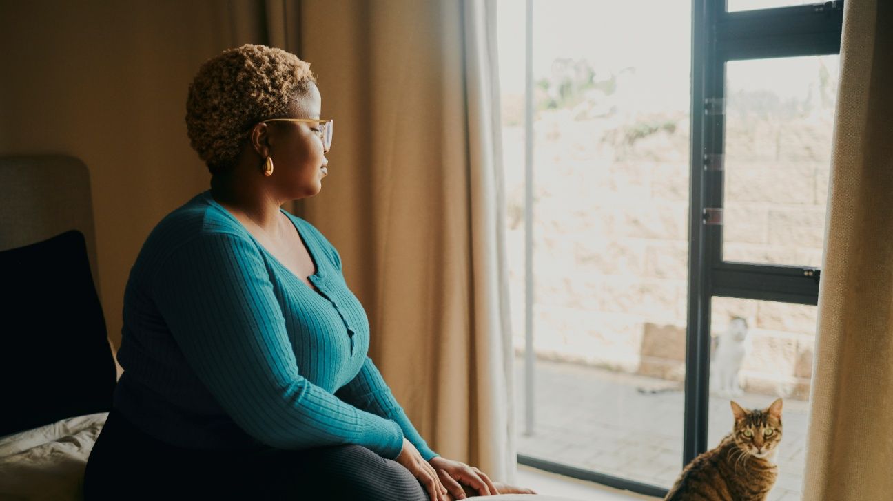 Female sitting on her bed, looking out the window with her cat
