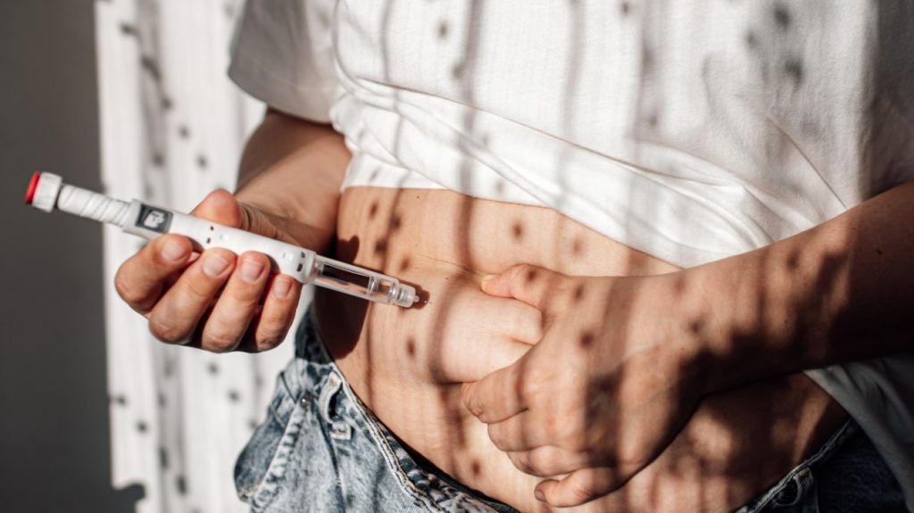close-up of woman self-administering GLP-1 injection into the abdomen with a pen syringe