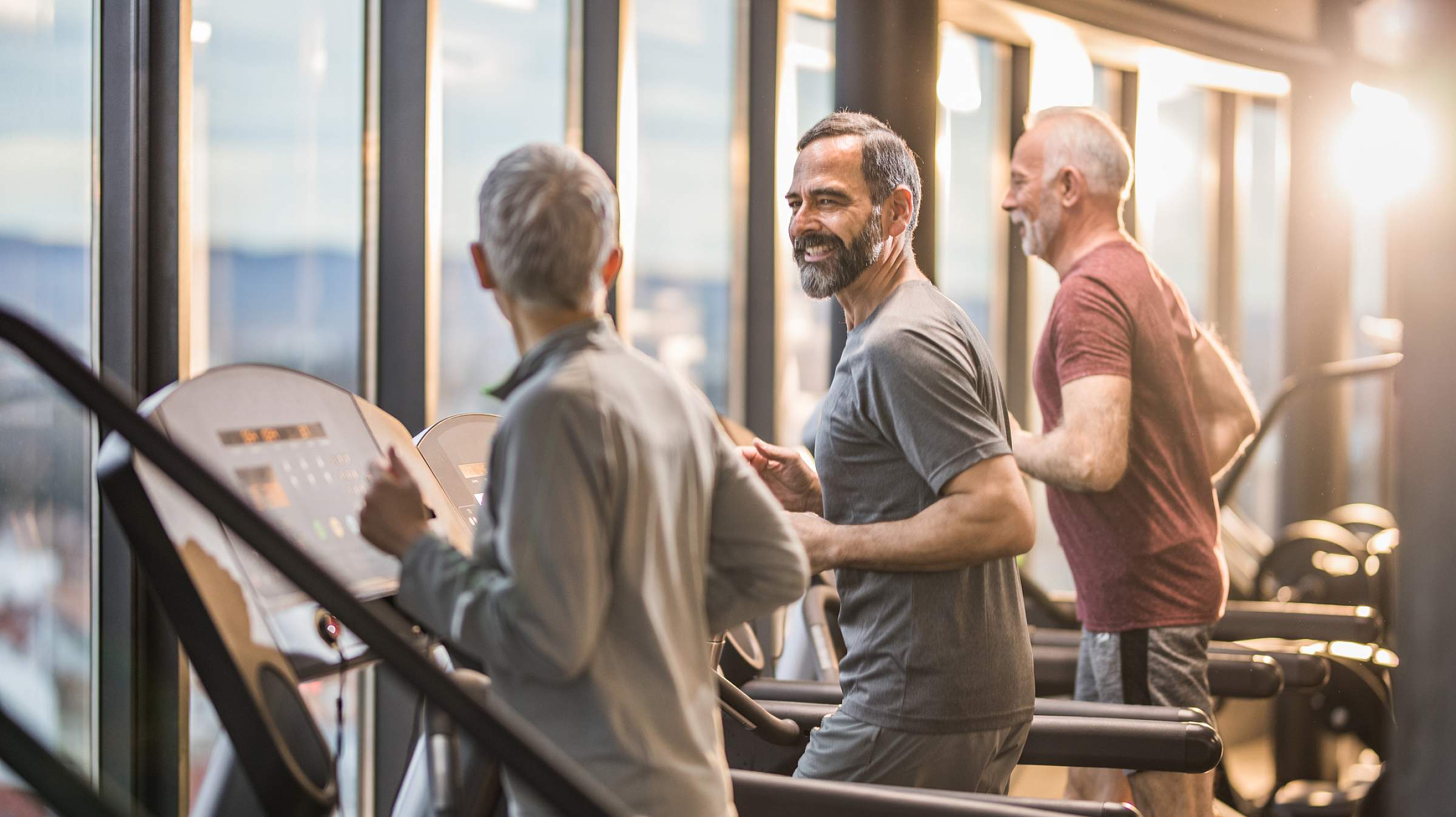 group of older men talking while warming up on treadmills in a gym