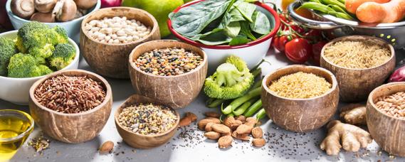 Assorted high-fiber foods in bowls on table, like broccoli, beans, nuts and leafy greens