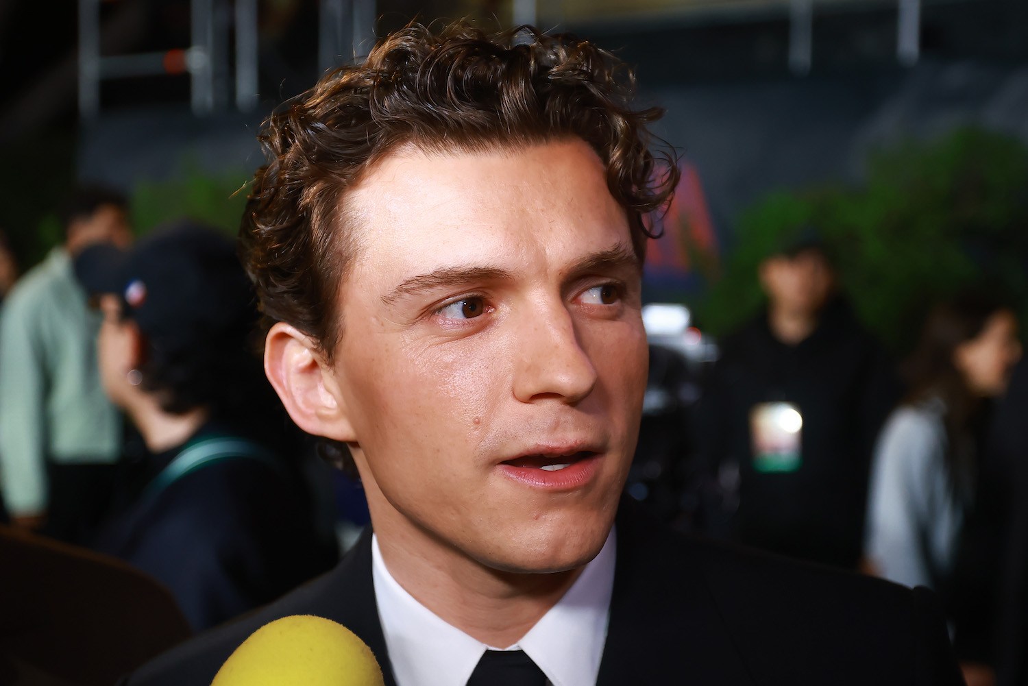 A close-up image of Tom Holland speaking into a microphone.