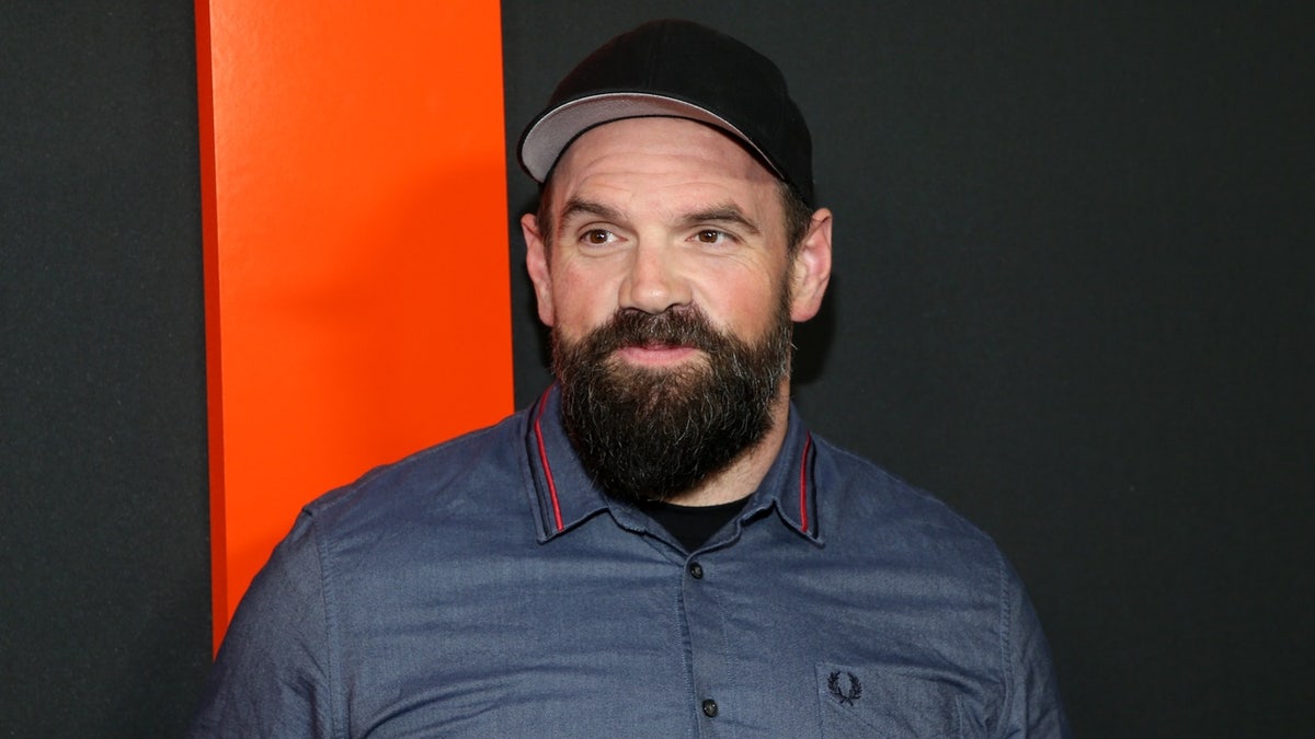 Ethan Suplee poses at a Hollywood event wearing a blue shirt, black baseball cap and beard.