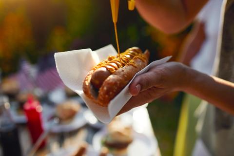 Person squeezing mustard onto their hotdog in a bun