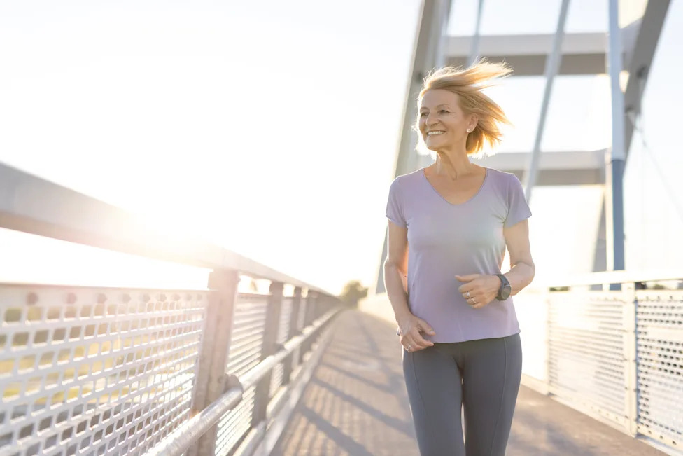 Woman jogging outdoors on a sunny bridge to support heart health and cardiovascular fitness