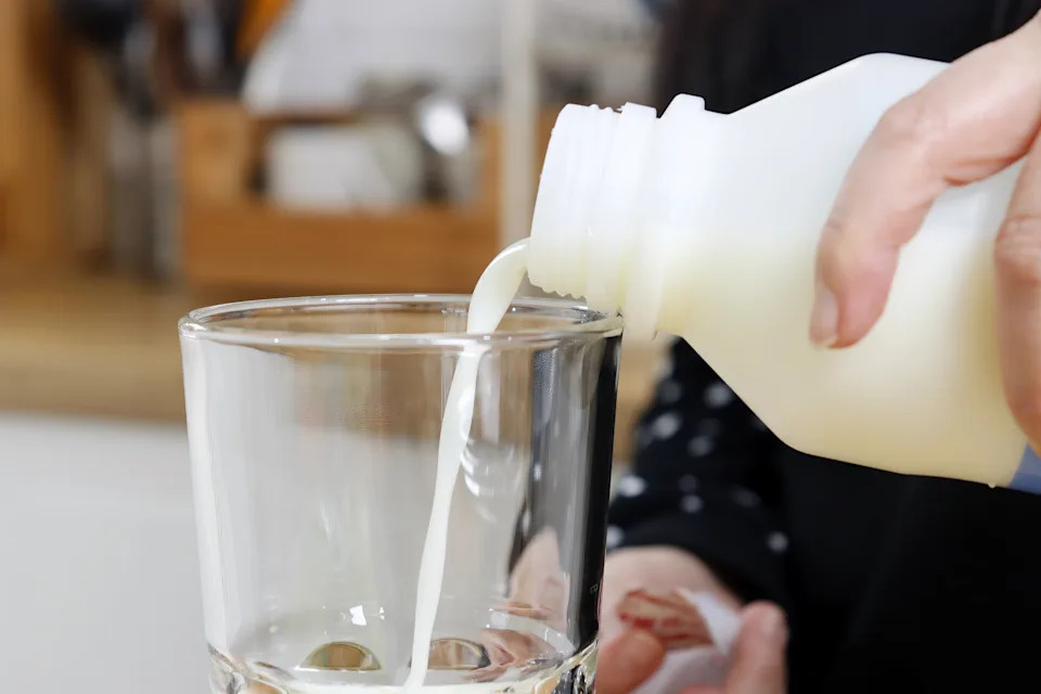 Woman Pouring Dairy Milk into a Drinking Glass in a Bright Kitchen Environment for Daily Nutrition Concept