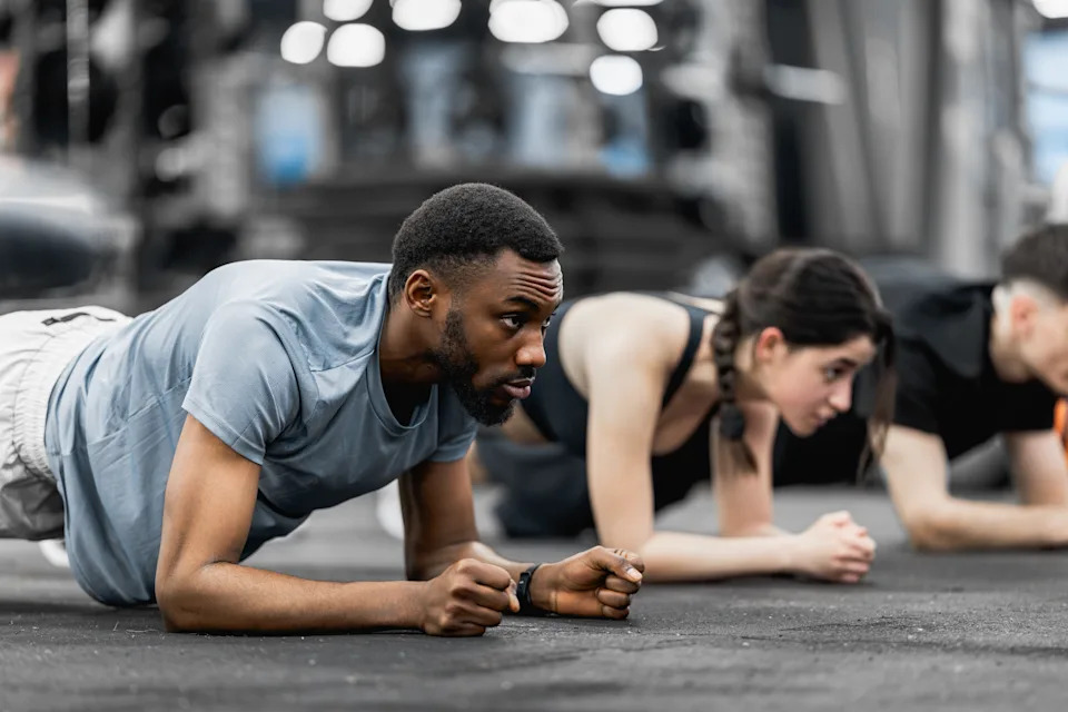 Group of young athletes performing plank workout in a gym, focused on core strength, endurance and teamwork during a guided training session with determination and intensity.
