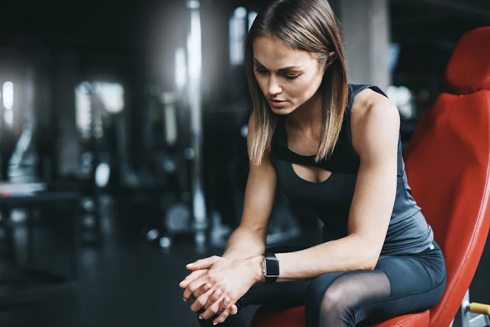 Woman sitting on gym bench looking tired during workout routine