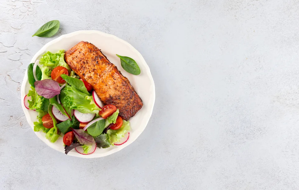 Grilled salmon fillet with fresh leafy greens, cherry tomatoes, radish on white background. Top view. High quality photo