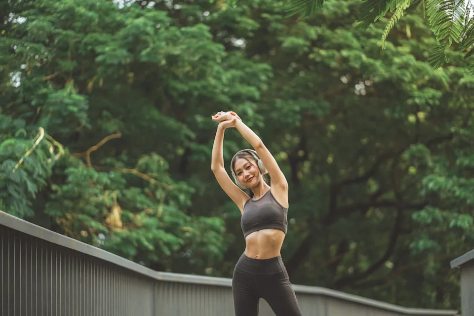 Woman stretching outdoors with headphones before a workout, representing morning exercise and weight loss benefits