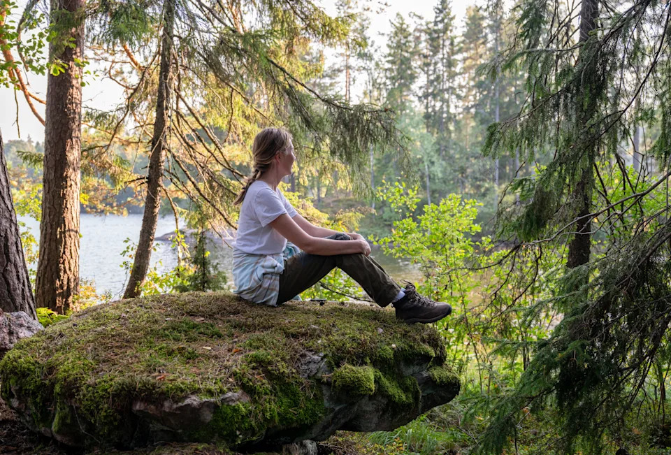 A young woman sitting on mossy rock surrounded by trees