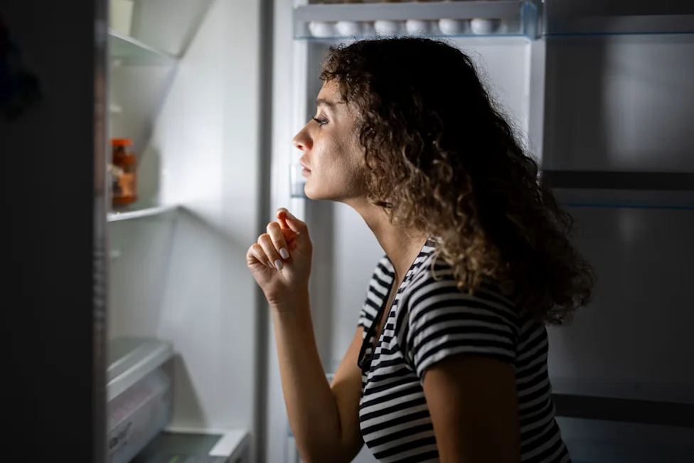 Woman looking inside an open refrigerator while deciding what to eat.