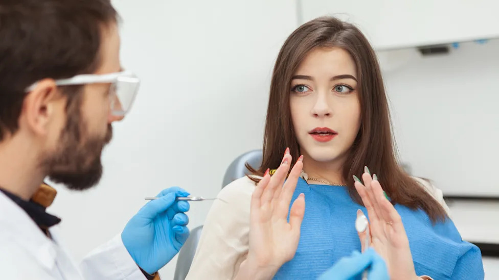 Young woman looking scared and nervous sitting in dental chair in front of her dentist. Terrified woman afraid of dental treatment
