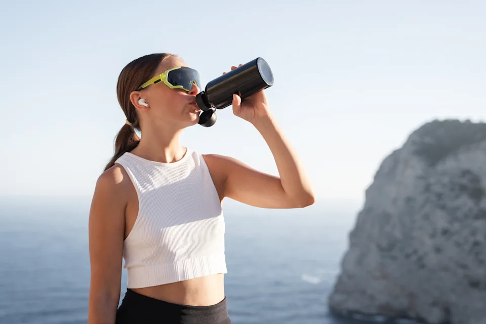 Woman drinking from a water bottle during an outdoor workout in sunny weather.