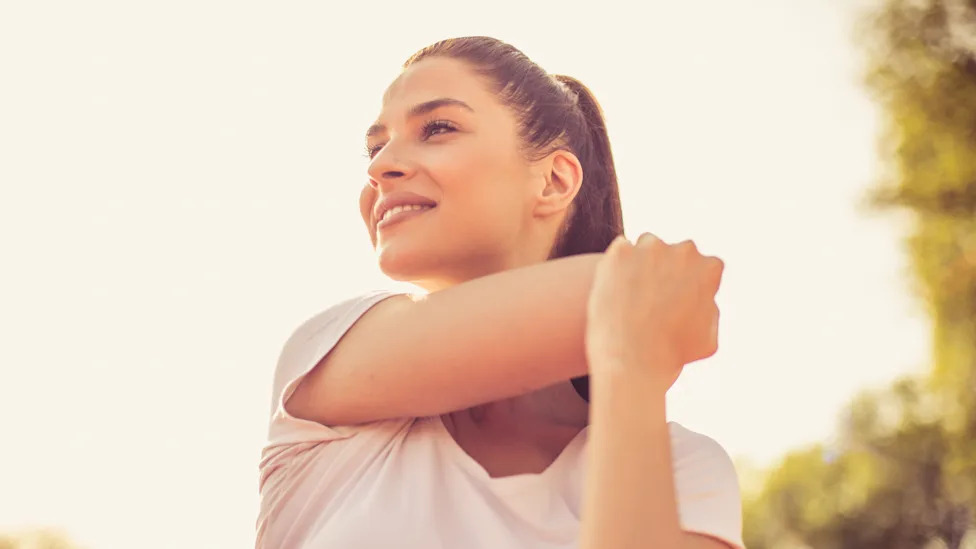 Woman stretching on an outdoor path in morning sunlight for brain health benefits
