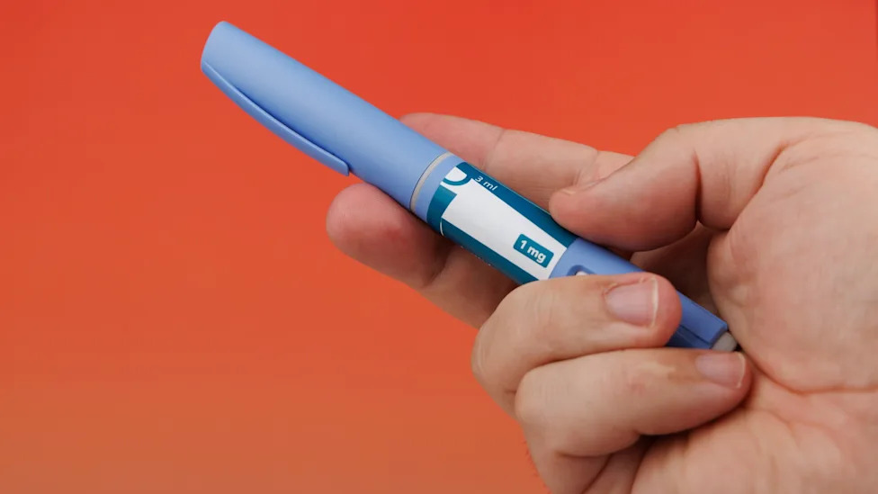 Horizontal photo of a hand holding several semaglutide injection pens used for diabetes and weight loss.