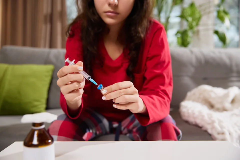 Woman holding a GLP-1 injection pen near her abdomen at home