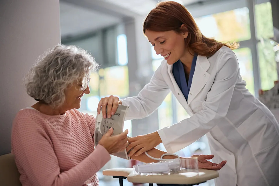 A doctor measures a seated patient's blood pressure with an arm cuff.