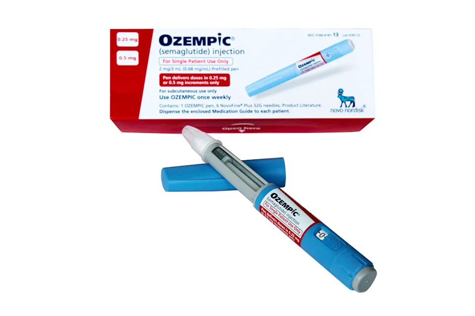 Hand holding an Ozempic semaglutide injection pen beside its weekly-dose box