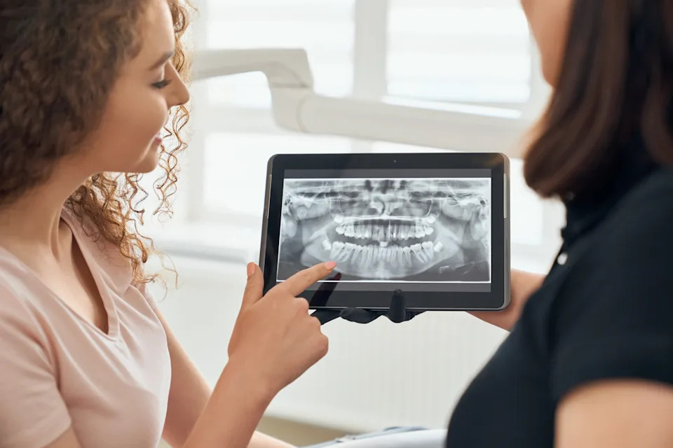 Dentist reviewing a dental X-ray on a tablet with a patient while explaining a periodontal treatment plan