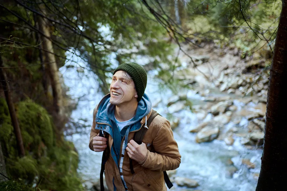 A man hikes near a river while smiing at a tree