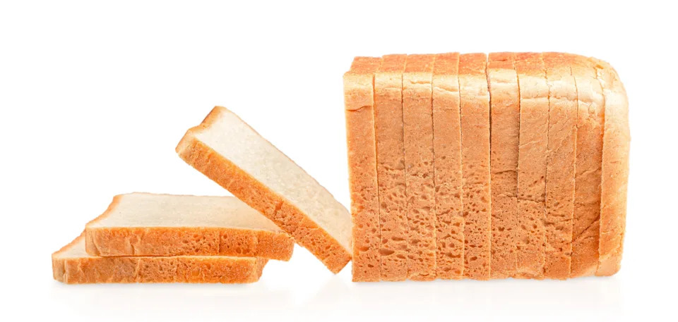 Sliced loaf of white bread with several slices arranged beside it on a white background.