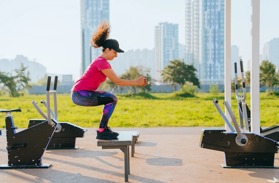 Woman doing squats at an outdoor fitness area in the morning sunlight.