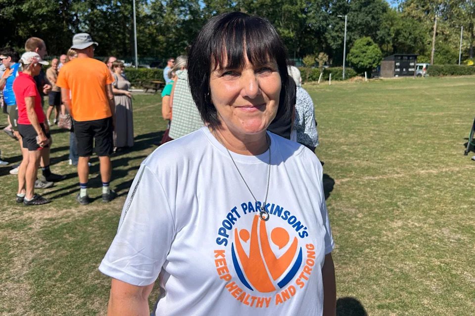 Annie Booth stands on a sports field wearing a white Sport Parkinson's T-shirt.