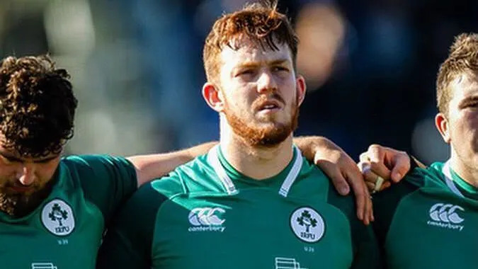 Ciaran Booth stands with teammates wearing a green Ireland rugby shirt before a match.