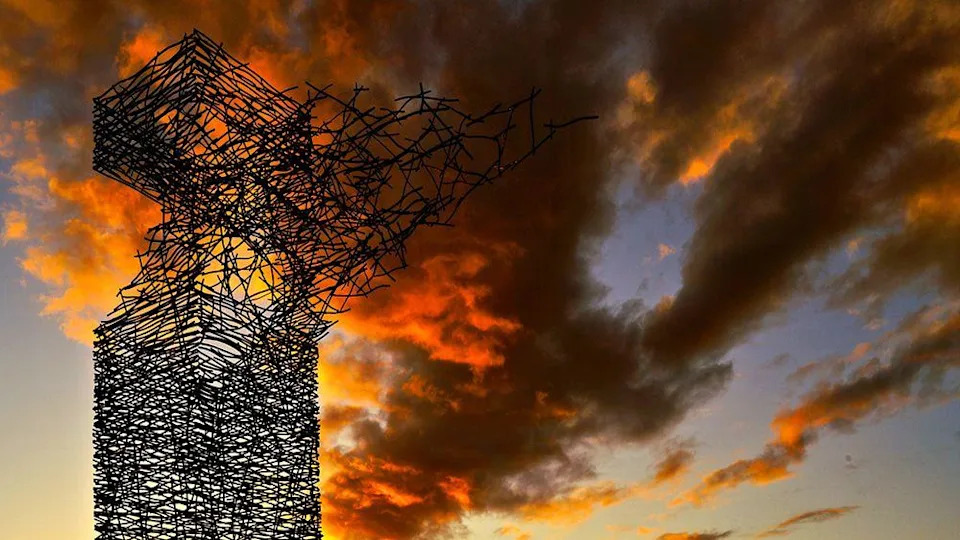The Airdrie Sky Tower stands in silhouette against a dramatic sunset sky, with vivid orange and red clouds illuminated by the setting sun.
