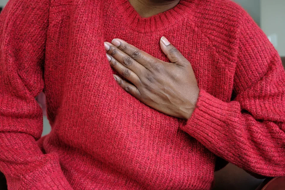 Person in a sweater holding their chest, suggesting heart-related health concerns