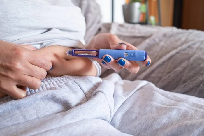 Person preparing to self-administer an injection in their abdomen while sitting on a couch