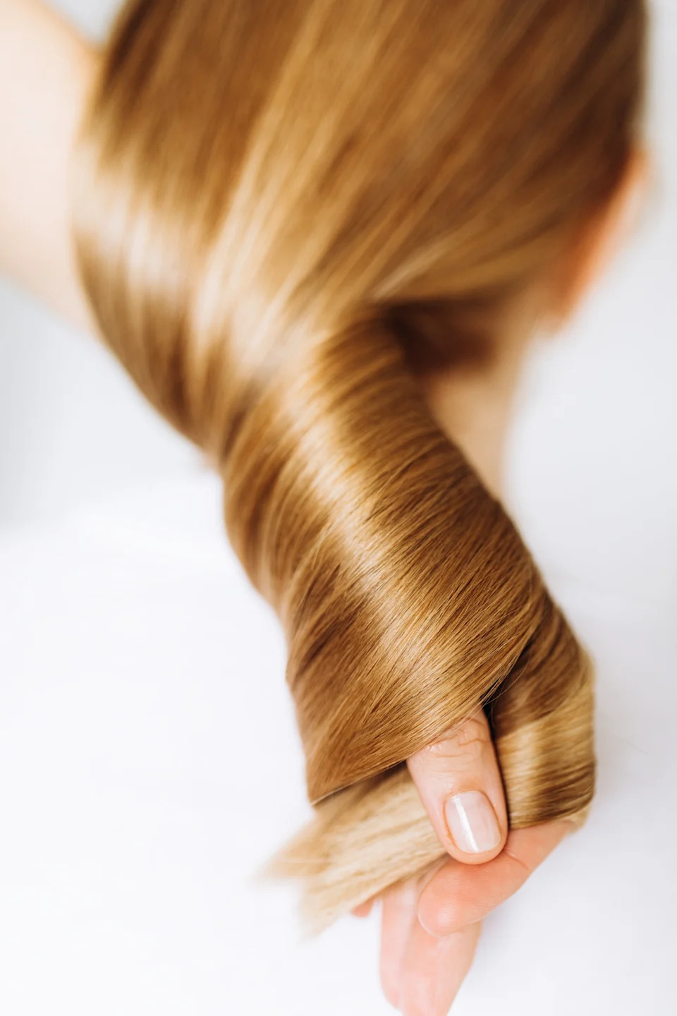 Close-up of a person's hand holding shiny, smooth hair, illustrating healthy hair care