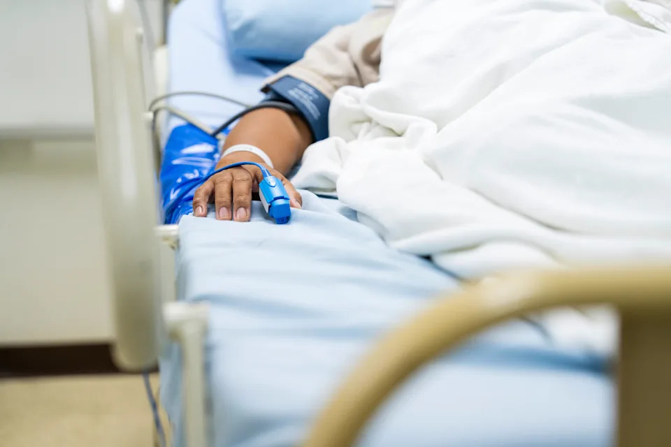 Person in hospital bed with IV and pulse oximeter on finger, suggesting a medical setting