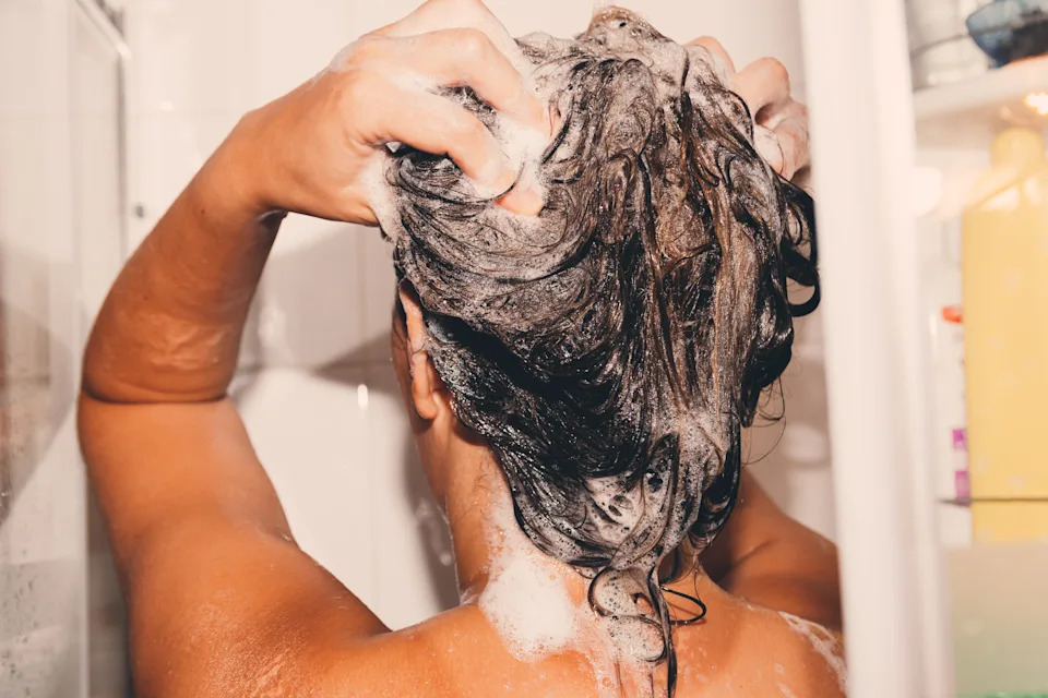 Person washing hair in the shower, massaging shampoo into their scalp