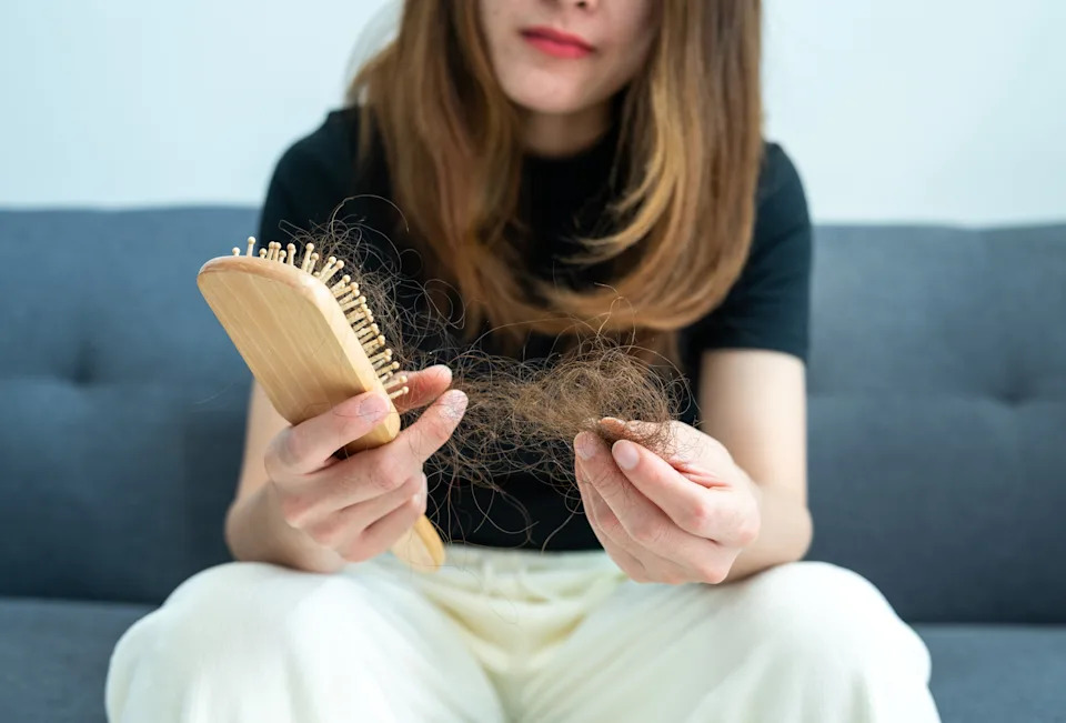 A person holds a hairbrush and a clump of hair, possibly indicating hair loss or health concerns