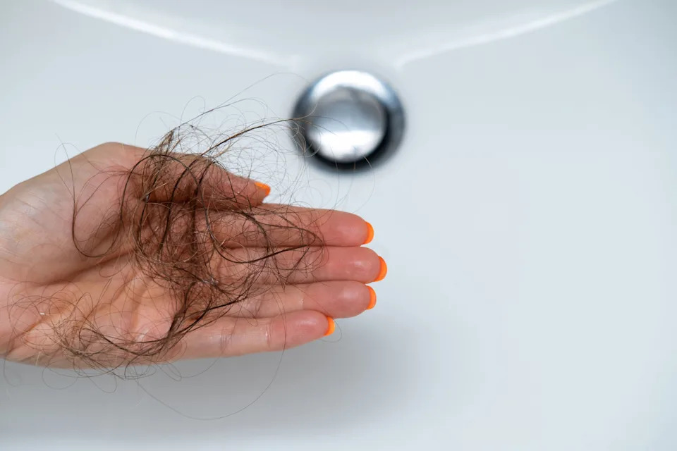Person holding a clump of hair over a bathroom sink, implying hair loss