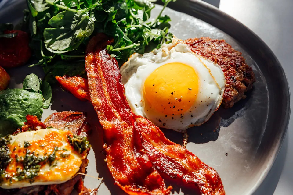 A plate with bacon, fried egg, and greens