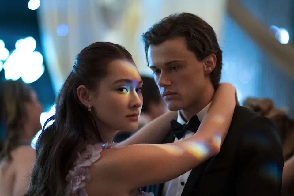 A couple embraces intimately at a formal event, the woman in an elegant floral dress and the man in a classic tuxedo