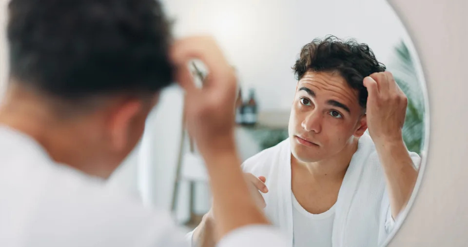 Person wearing a robe looks in the mirror, adjusting their hair, possibly focusing on hair health or style