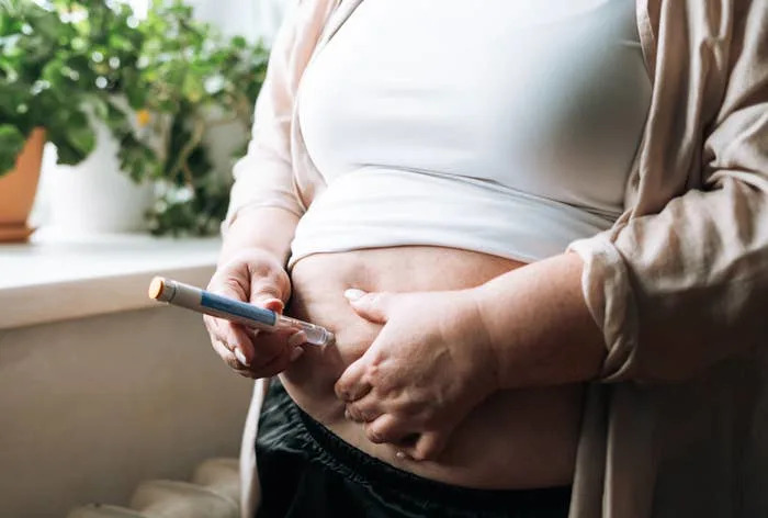 Person self-administers an injection in the abdomen area at home, highlighting self-care or medical treatment