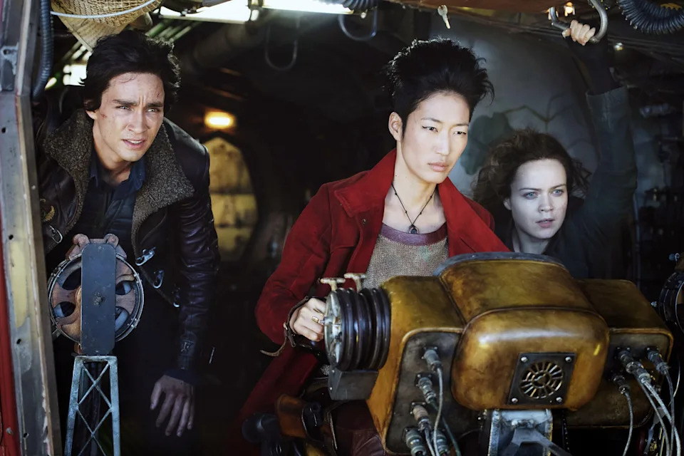 Three characters intensely focus while operating a complex control panel in a vehicle, suggesting a scene from an action or adventure film