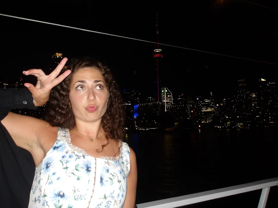 A person playfully poses in front of a nighttime city skyline with a lit tower