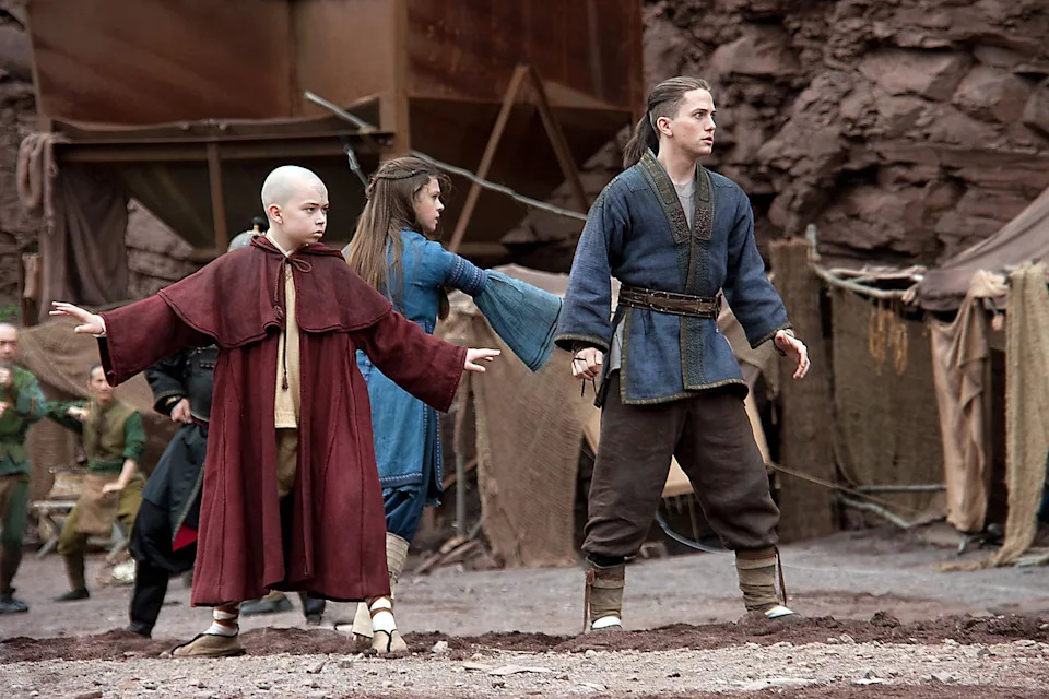 Characters in fantasy costumes pose dramatically in a rocky, barren setting